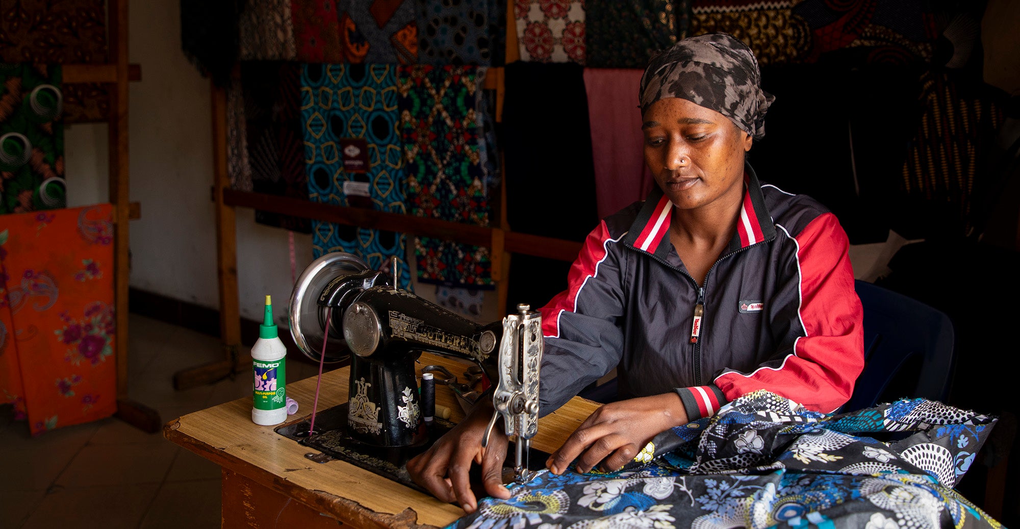 A woman sews bags in a Tanzania shop surrounded by colorful fabrics.
