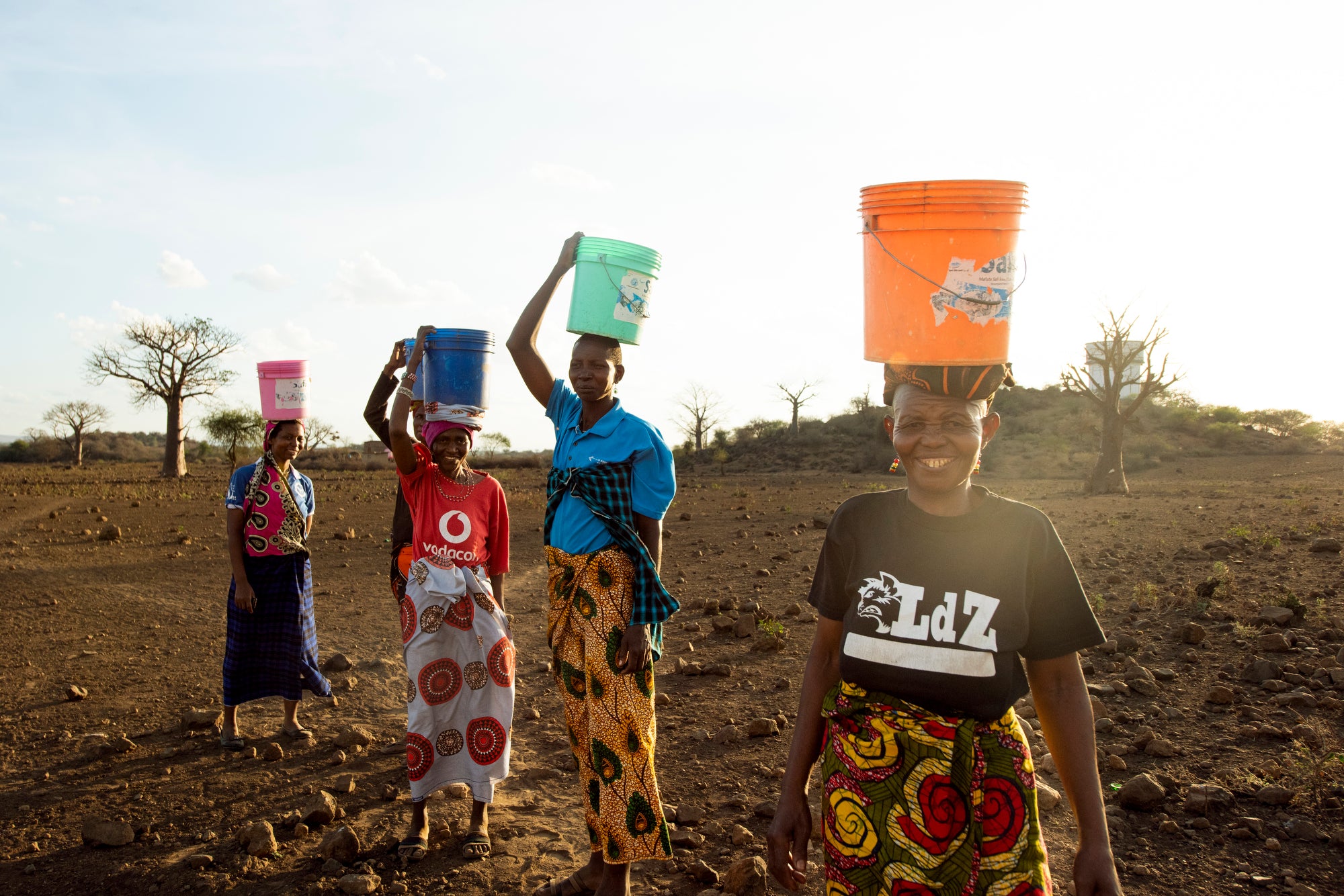 African women walk with buckets on their heads to carry water home.