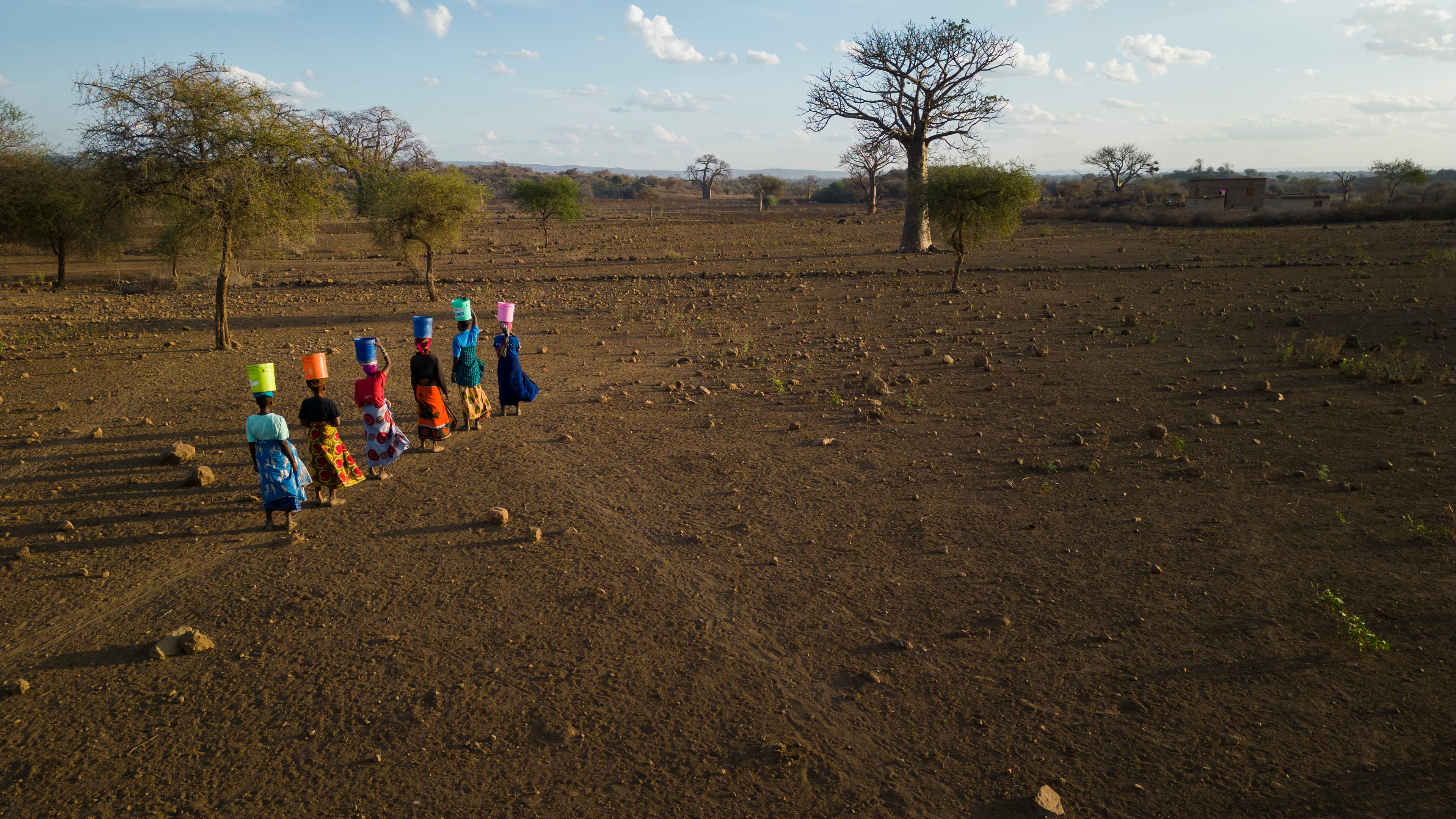 Women walk for water with colorful buckets on their heads in Tanzania.